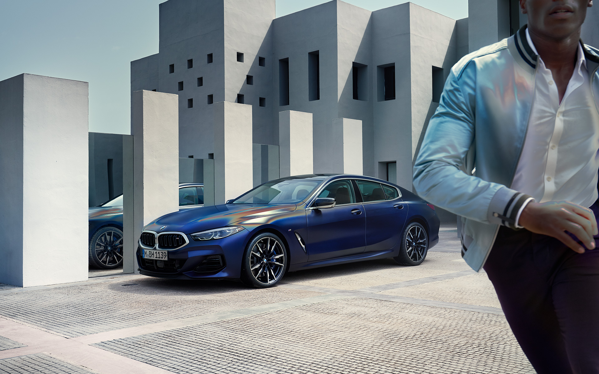 BMW M850i xDrive Gran Coupé G16 LCI Facelift 2022 BMW Individual Frozen Tanzanite Blue metallic three-quarter front view standing with male model in foreground