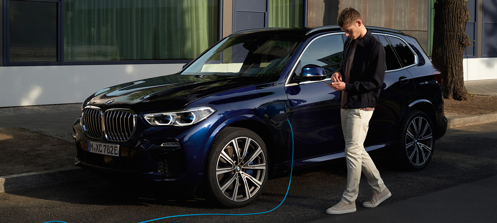 Man uses My BMW App from BMW ConnectedDrive on smartphone while charging his BMW X5 Plug-in Hybrid